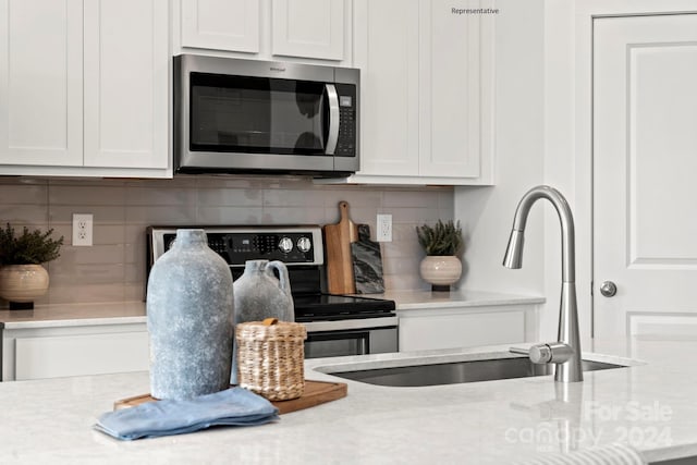 kitchen with stainless steel appliances, sink, backsplash, light stone countertops, and white cabinetry