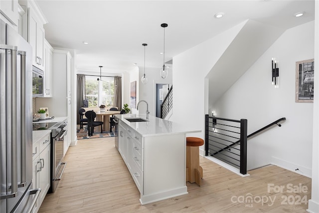 kitchen with hanging light fixtures, white cabinetry, a kitchen island with sink, light hardwood / wood-style flooring, and stainless steel appliances