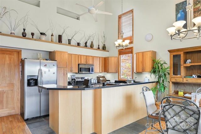 kitchen featuring a towering ceiling, appliances with stainless steel finishes, hanging light fixtures, dark wood-type flooring, and ceiling fan with notable chandelier