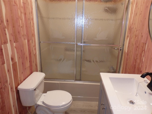 full bathroom with combined bath / shower with glass door, toilet, wooden walls, vanity, and hardwood / wood-style flooring