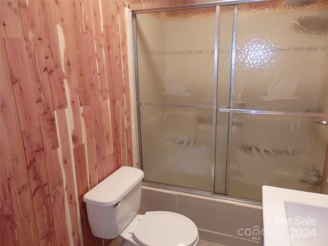 bathroom featuring wooden walls, bath / shower combo with glass door, and toilet