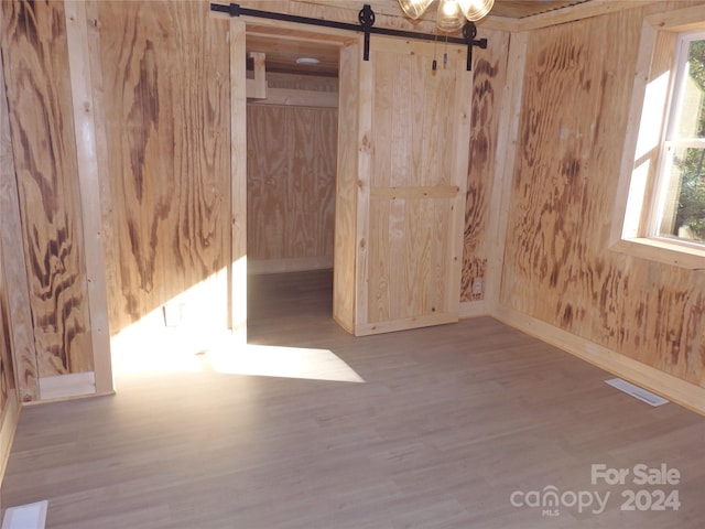 empty room featuring hardwood / wood-style floors, a barn door, and wood walls