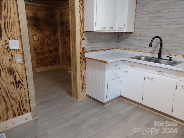 kitchen featuring light hardwood / wood-style floors, sink, wooden walls, and white cabinets