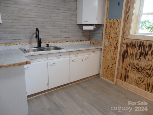 kitchen featuring electric panel, white cabinetry, wood walls, light hardwood / wood-style floors, and sink