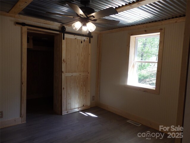 unfurnished bedroom with wood finished floors, baseboards, visible vents, and a barn door