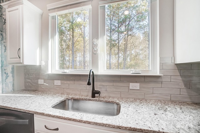 kitchen with sink, light stone countertops, black dishwasher, tasteful backsplash, and white cabinetry