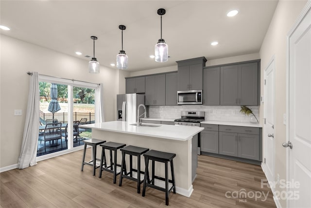 kitchen with stainless steel appliances, a center island with sink, gray cabinetry, and sink