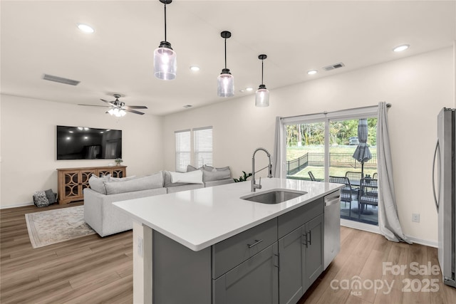 kitchen featuring stainless steel appliances, ceiling fan, a kitchen island with sink, sink, and pendant lighting