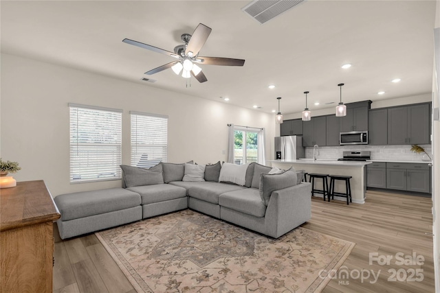 living room featuring ceiling fan, sink, and light hardwood / wood-style floors