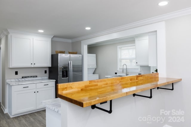 kitchen featuring stacked washer / dryer, wooden counters, white cabinetry, and stainless steel fridge