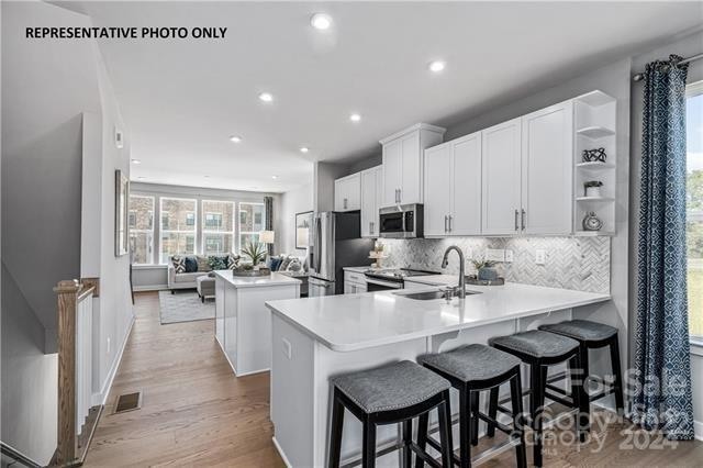 kitchen with appliances with stainless steel finishes, light wood-type flooring, a kitchen bar, kitchen peninsula, and white cabinets