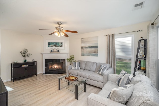 living room with ceiling fan, a tile fireplace, and light hardwood / wood-style floors