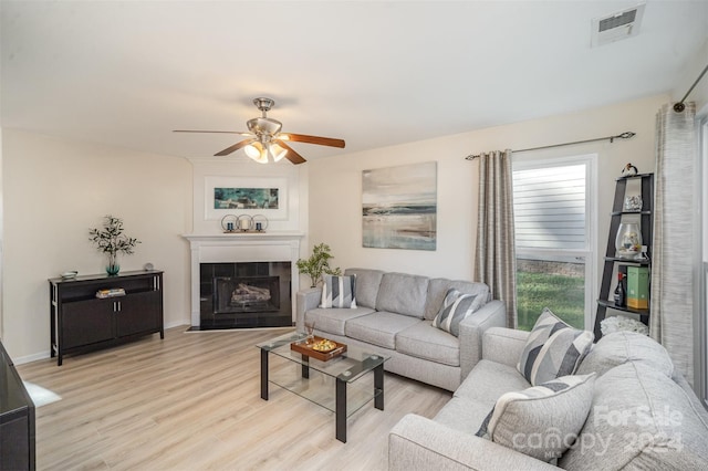 living room featuring ceiling fan, a tile fireplace, and light wood-type flooring