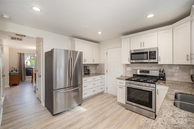 kitchen featuring light hardwood / wood-style flooring, light stone countertops, white cabinets, and stainless steel appliances