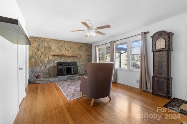 living room with a wood stove, light hardwood / wood-style floors, and ceiling fan