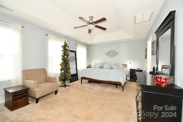 bedroom with a raised ceiling, light colored carpet, and ceiling fan