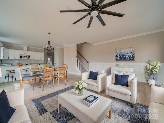 living room featuring crown molding, ceiling fan with notable chandelier, and light hardwood / wood-style flooring