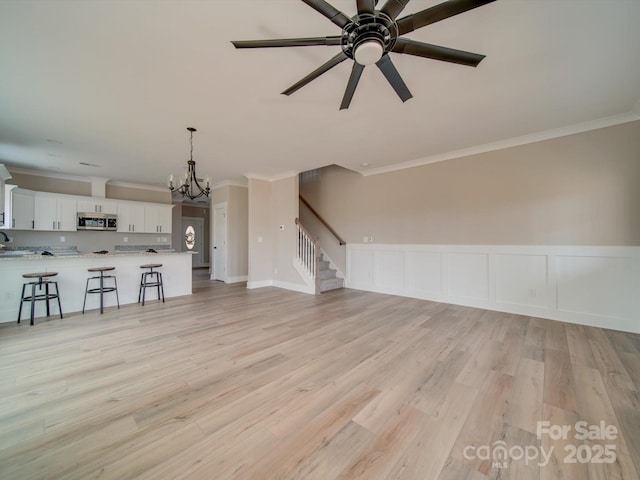 unfurnished living room with ceiling fan with notable chandelier, light hardwood / wood-style flooring, and crown molding