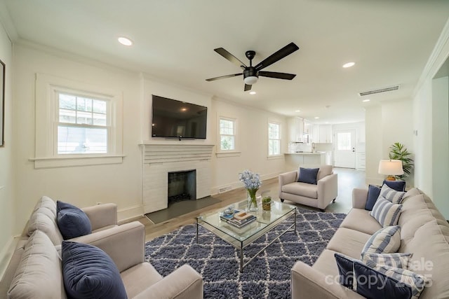 living room featuring hardwood / wood-style floors, ceiling fan, a premium fireplace, and crown molding