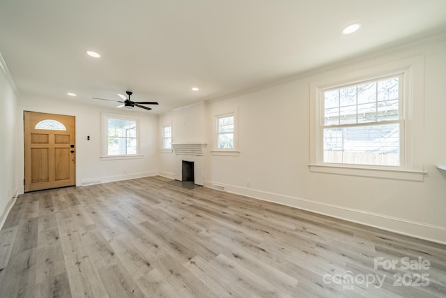 unfurnished living room with ceiling fan, a fireplace, crown molding, and light wood-type flooring