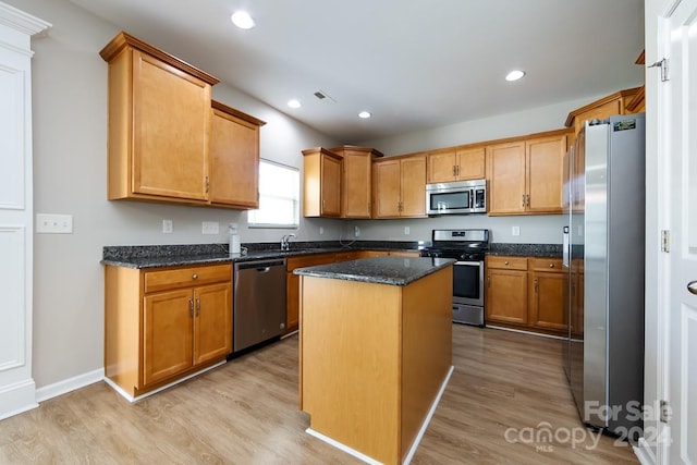 kitchen with light hardwood / wood-style flooring, a kitchen island, dark stone counters, and appliances with stainless steel finishes