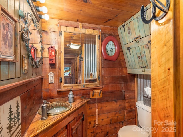 half bathroom featuring wood ceiling, toilet, vanity, and wooden walls
