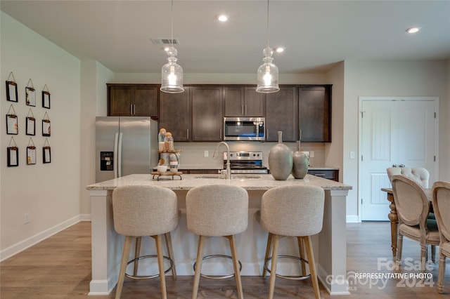 kitchen with hardwood / wood-style floors, appliances with stainless steel finishes, sink, and a kitchen island with sink