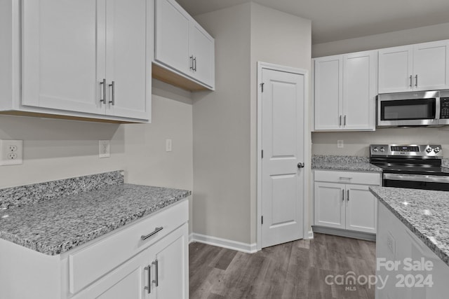 kitchen with white cabinets, light stone counters, stainless steel appliances, and light hardwood / wood-style floors