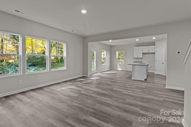 unfurnished living room featuring a healthy amount of sunlight, sink, and light wood-type flooring