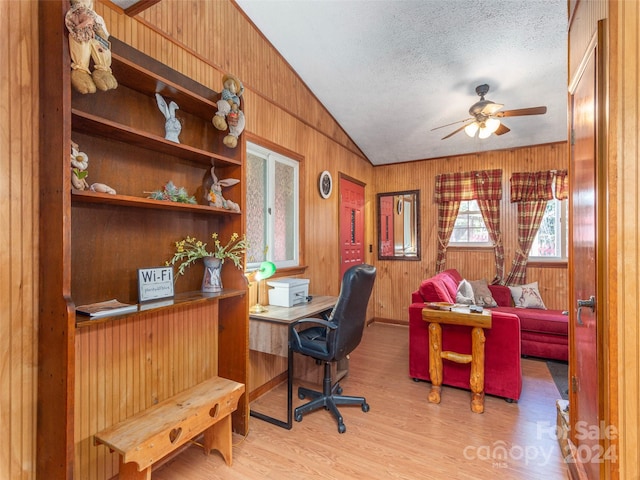 home office with light hardwood / wood-style floors, built in desk, ceiling fan, a textured ceiling, and wooden walls