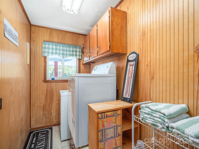 clothes washing area with cabinets, wood walls, light tile patterned floors, and independent washer and dryer