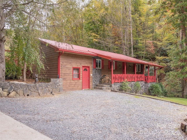 view of front of property featuring a wooded view, driveway, metal roof, and covered porch