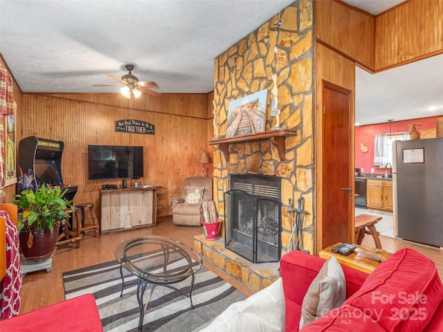 living area featuring ceiling fan, wood walls, wood finished floors, and a stone fireplace