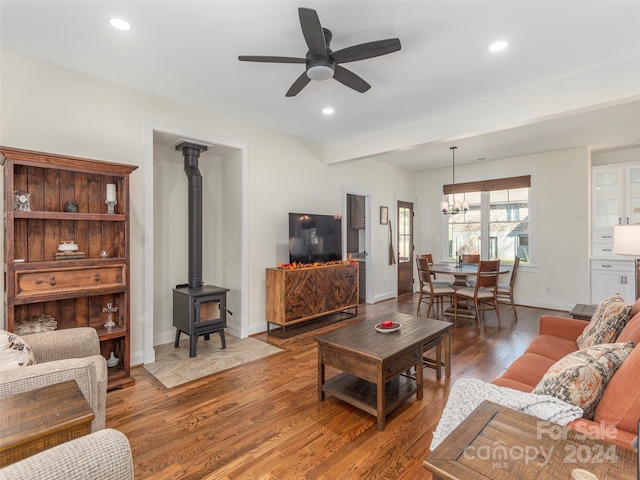 living room featuring a wood stove, wood-type flooring, and ceiling fan with notable chandelier