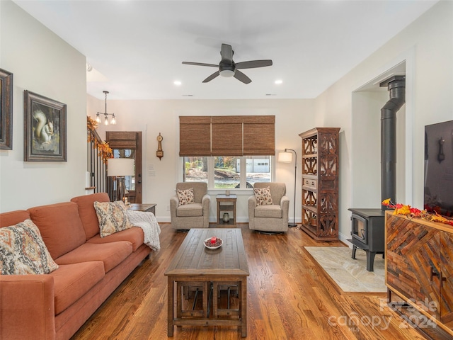 living room featuring a wood stove, wood-type flooring, and ceiling fan with notable chandelier