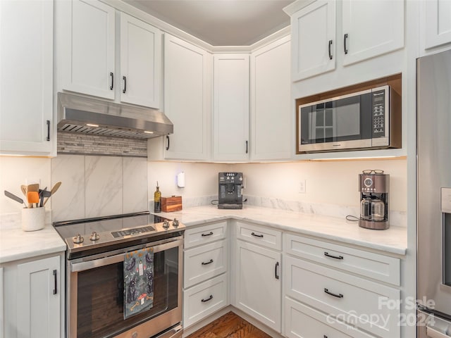 kitchen with white cabinets, hardwood / wood-style flooring, light stone countertops, appliances with stainless steel finishes, and tasteful backsplash