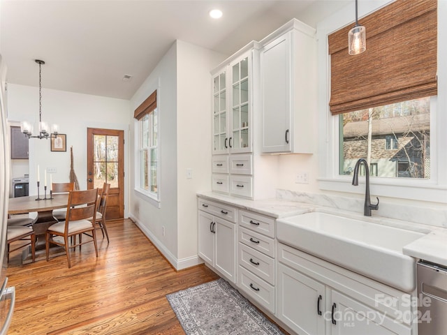 kitchen with light stone countertops, white cabinetry, sink, an inviting chandelier, and light hardwood / wood-style floors