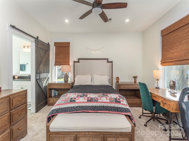 bedroom with ensuite bath, light colored carpet, ceiling fan, sink, and a barn door