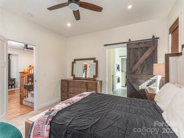 bedroom with a barn door, light hardwood / wood-style flooring, and ceiling fan