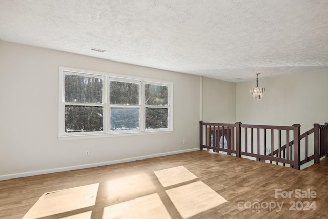 unfurnished room with light hardwood / wood-style floors, a textured ceiling, and a notable chandelier