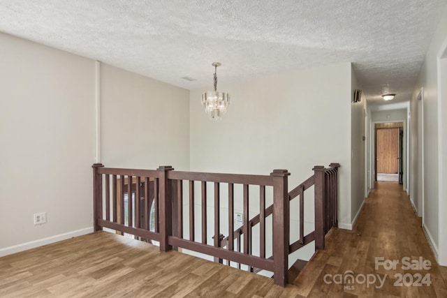 corridor featuring hardwood / wood-style floors, a notable chandelier, and a textured ceiling