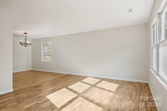 unfurnished room with a chandelier, a textured ceiling, and hardwood / wood-style flooring