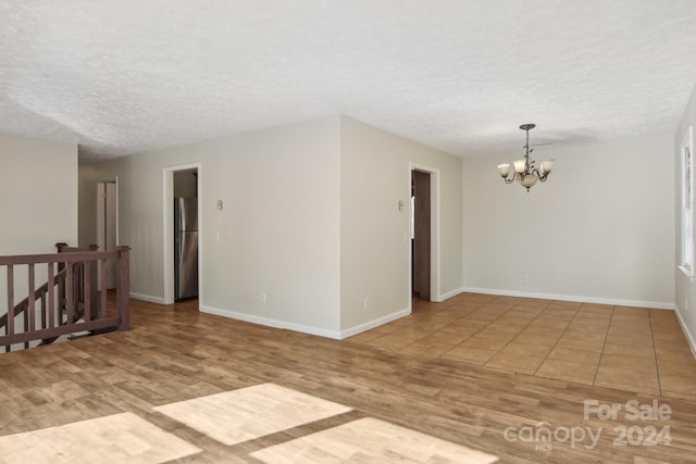 empty room with light hardwood / wood-style flooring, a textured ceiling, and a notable chandelier