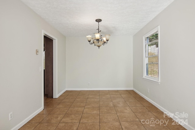 spare room featuring tile patterned floors, a textured ceiling, and a chandelier