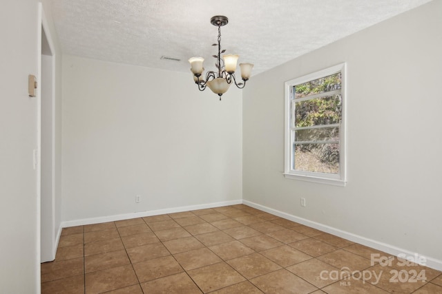 tiled spare room featuring a notable chandelier and a textured ceiling