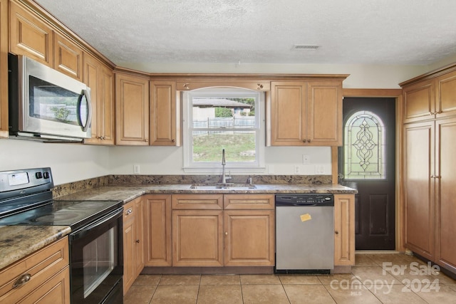 kitchen featuring sink, dark stone countertops, a textured ceiling, light tile patterned flooring, and stainless steel appliances