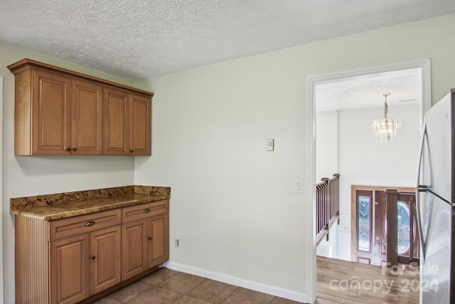 kitchen with hanging light fixtures, a textured ceiling, light tile patterned flooring, stainless steel refrigerator, and a chandelier