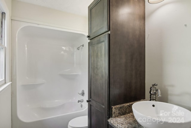 full bathroom with a textured ceiling, toilet, washtub / shower combination, and sink