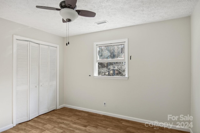 unfurnished bedroom featuring hardwood / wood-style flooring, ceiling fan, a textured ceiling, and a closet