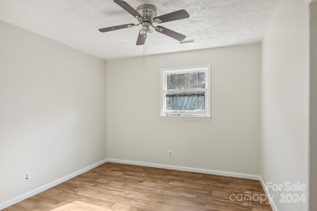 empty room featuring ceiling fan, light wood-type flooring, and a textured ceiling